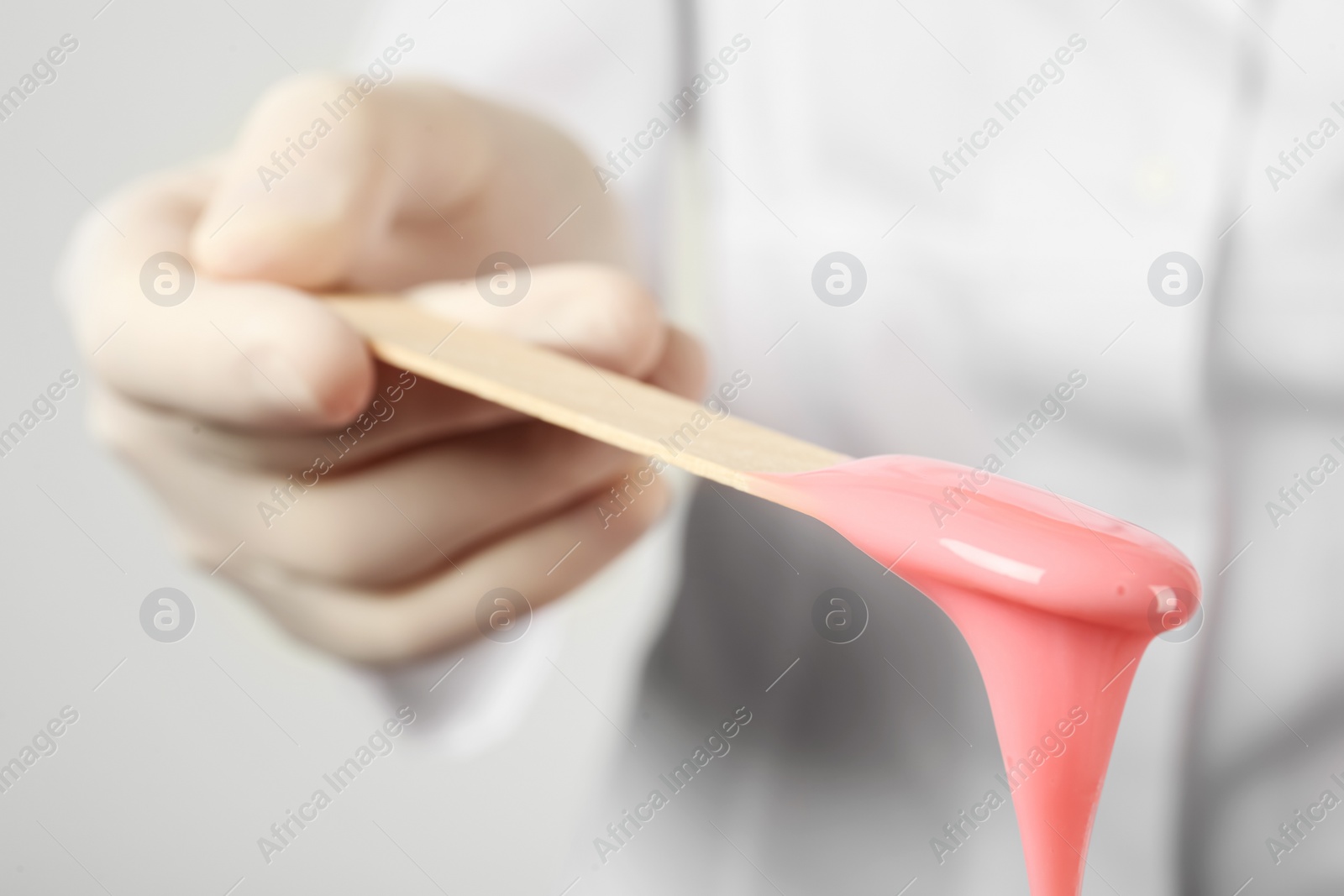 Photo of Woman holding spatula with hot depilatory wax, closeup