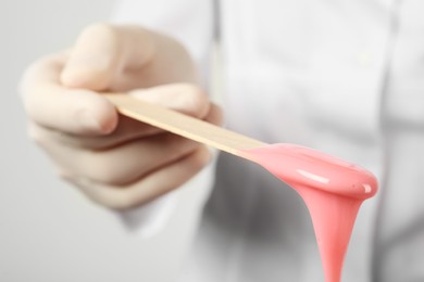 Woman holding spatula with hot depilatory wax, closeup