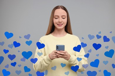 Image of Long distance love. Woman chatting with sweetheart via smartphone on grey background. Hearts around her