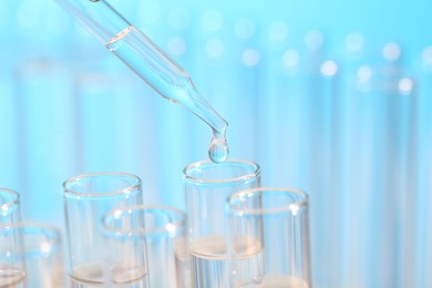 Photo of Laboratory analysis. Dripping liquid from pipette into glass test tube on light blue background, closeup and space for text