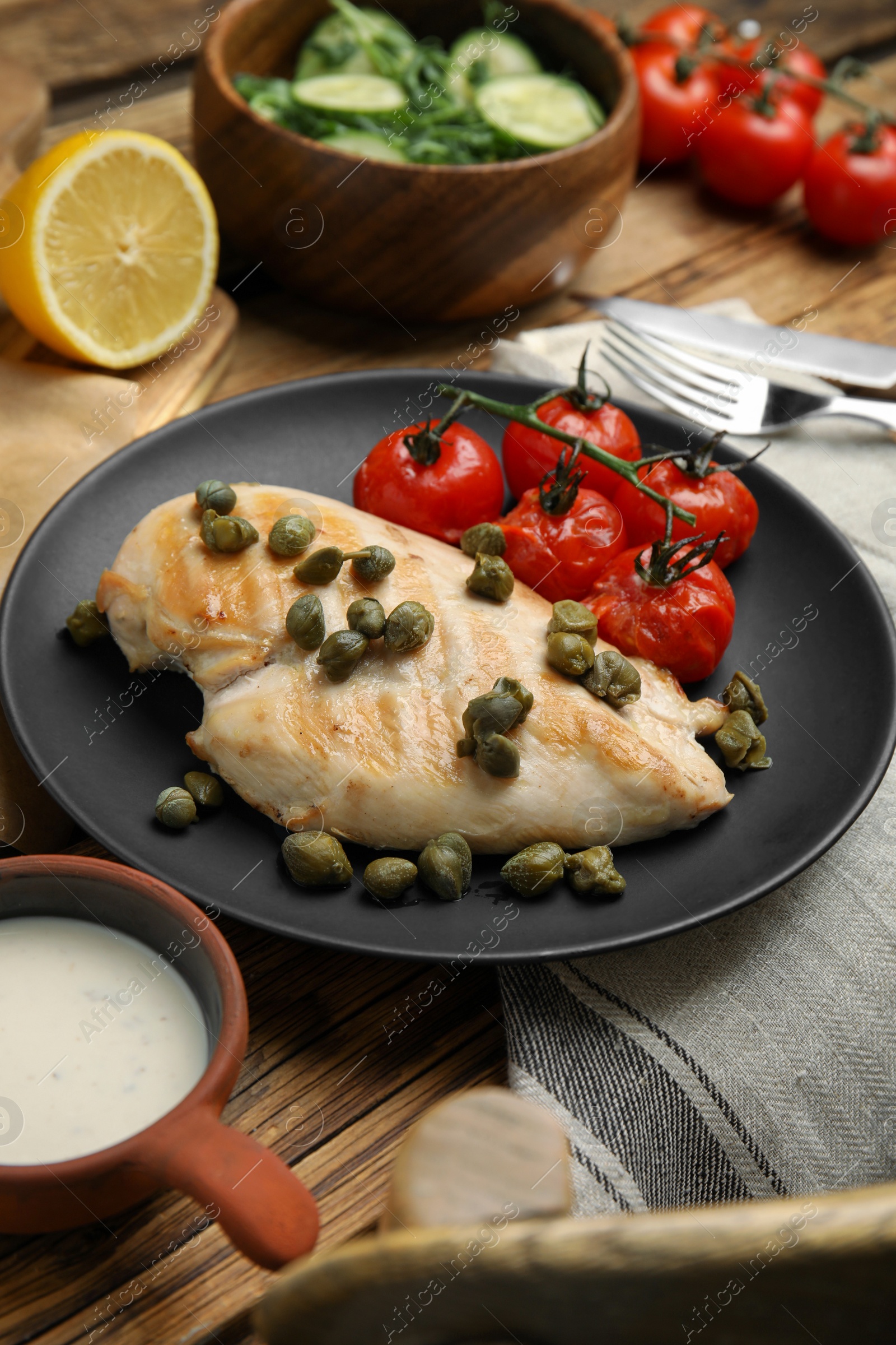 Photo of Delicious cooked chicken fillet with capers and tomatoes served on wooden table