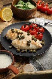 Delicious cooked chicken fillet with capers and tomatoes served on wooden table