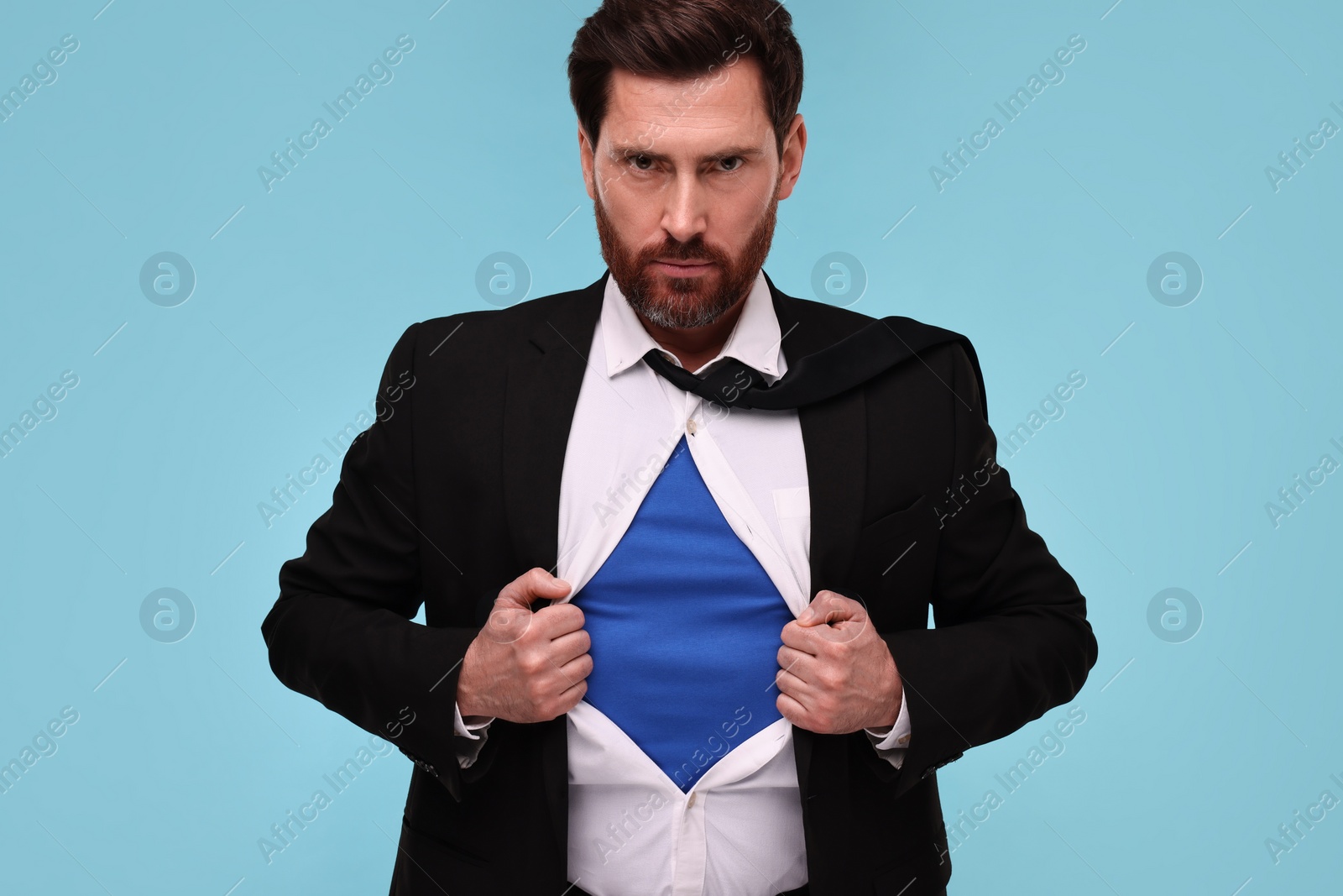 Photo of Confident businessman wearing superhero costume under suit on light blue background