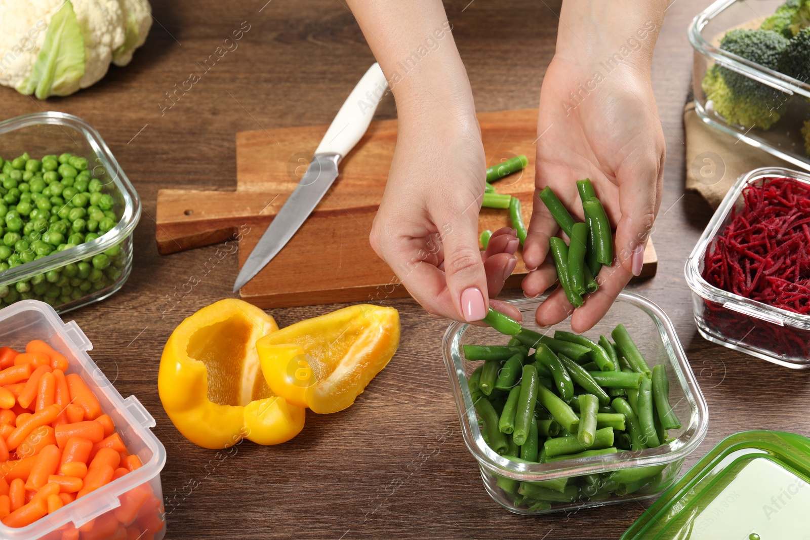 Photo of Woman putting green beans into glass container at wooden table, closeup. Food storage