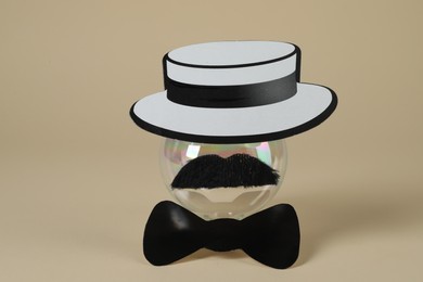 Photo of Man's face made of fake mustache, ball, hat and bow tie on beige background