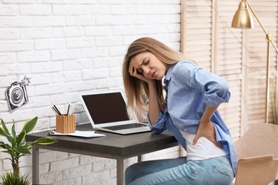 Photo of Young woman suffering from back pain in office