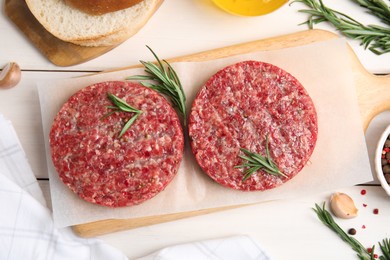 Raw hamburger patties with rosemary and pepper on white wooden table, flat lay