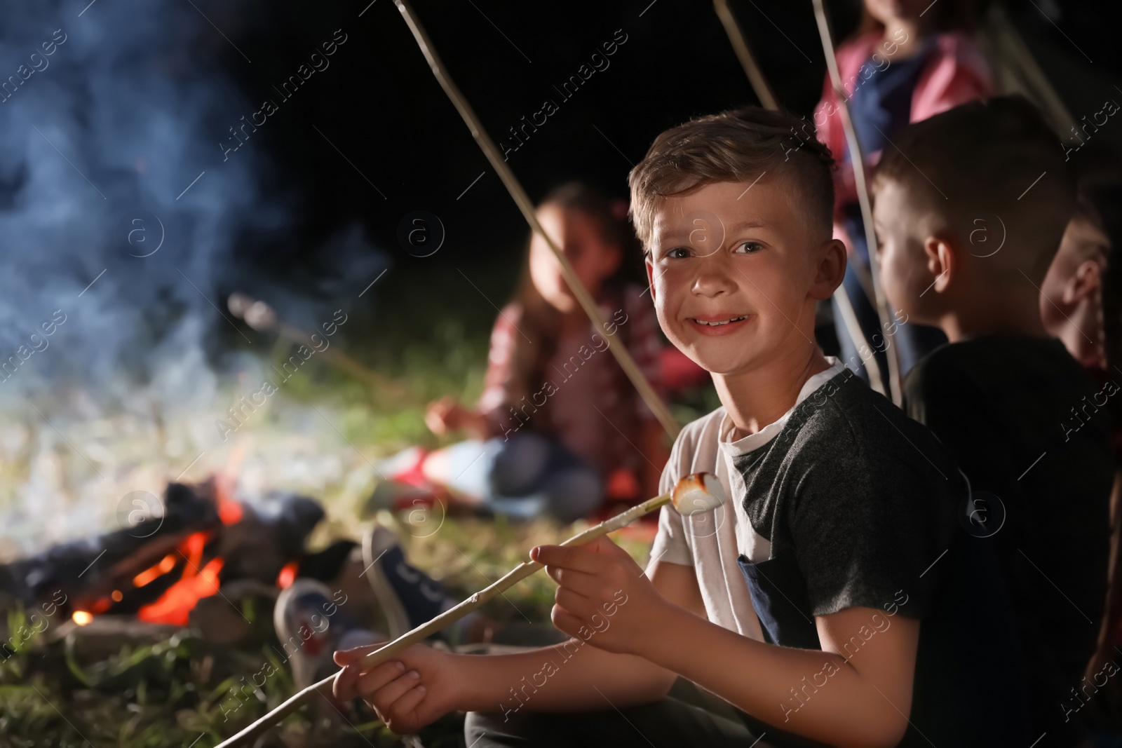 Photo of Little boy with marshmallow near bonfire at night. Summer camp