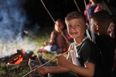 Little boy with marshmallow near bonfire at night. Summer camp