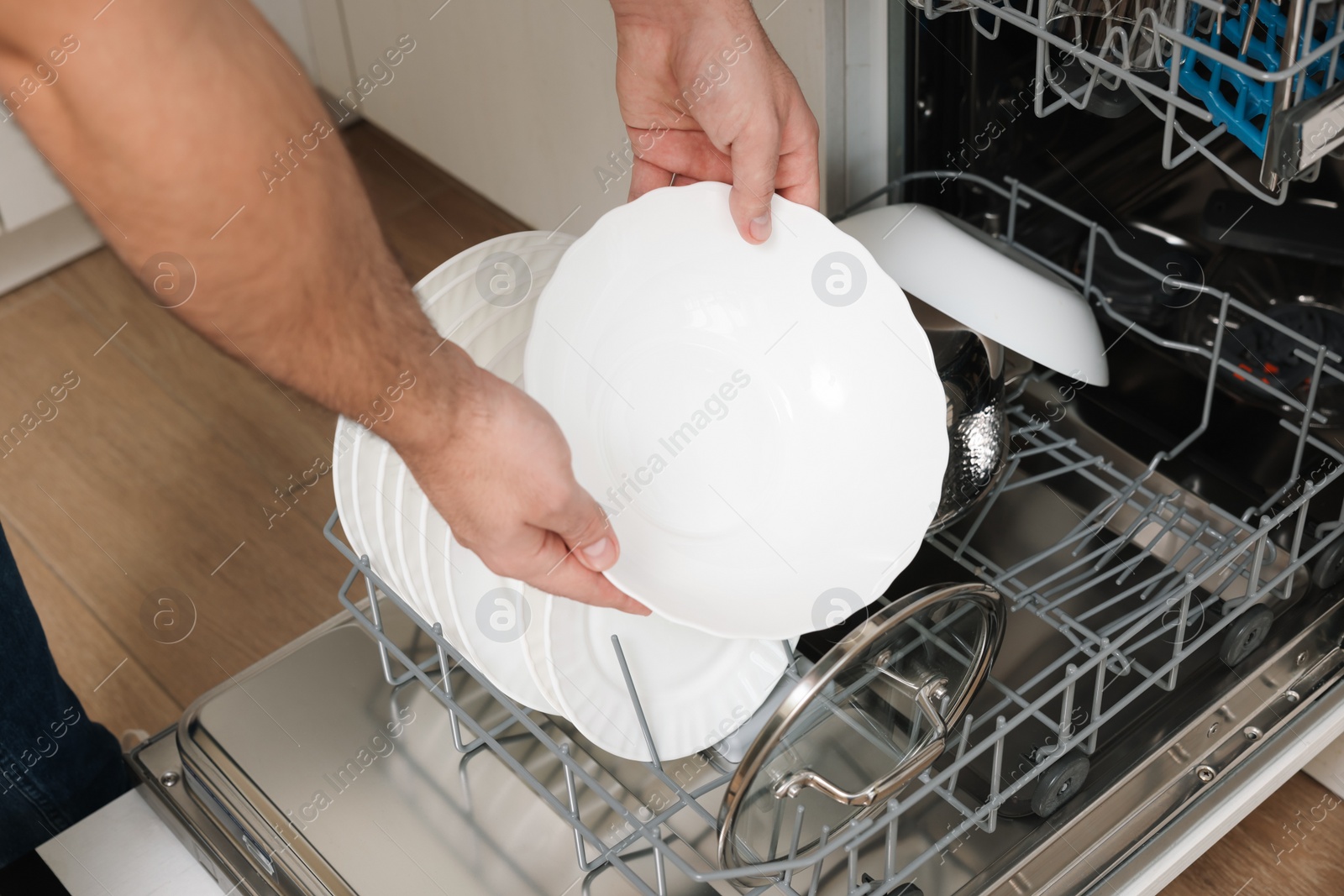 Photo of Man loading dishwasher with plates indoors, closeup