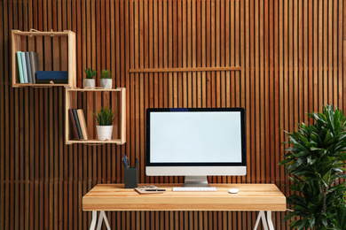 Comfortable workplace with computer near wooden wall in stylish room interior. Home office design