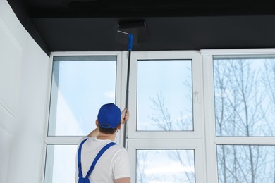 Photo of Worker in uniform painting ceiling with roller indoors