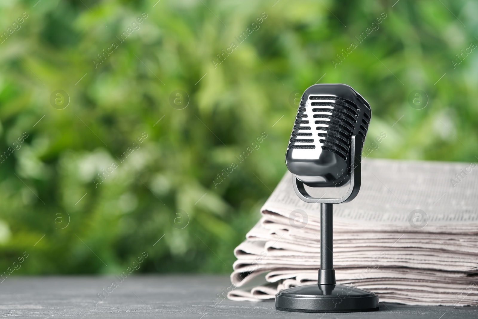 Photo of Newspapers and vintage microphone on grey table against blurred green background, space for text. Journalist's work