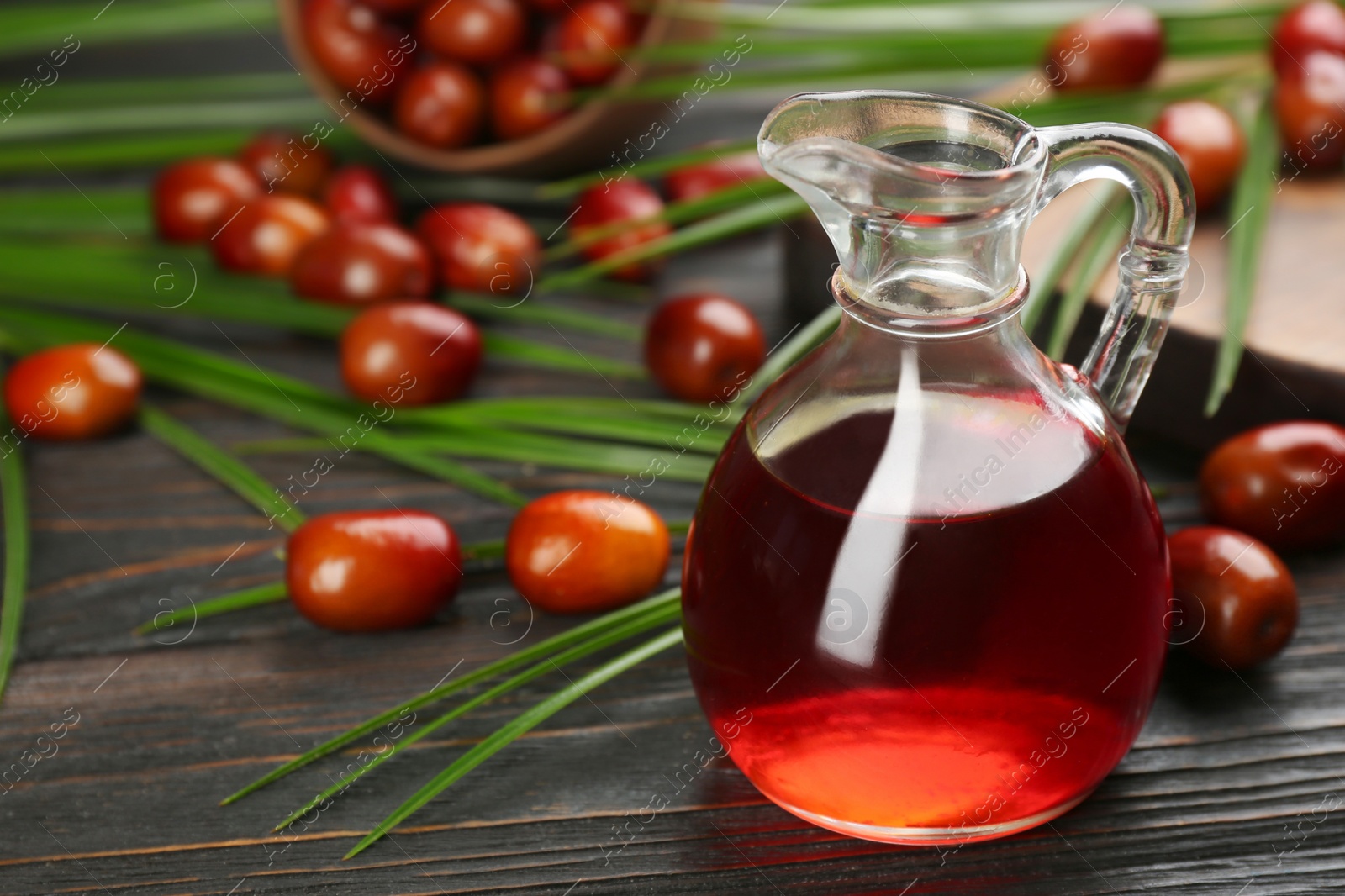 Photo of Palm oil in glass jug, tropical leaves and fruits on wooden table. Space for text