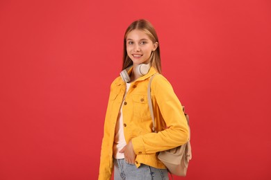Photo of Teenage student with backpack and headphones on red background
