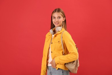 Teenage student with backpack and headphones on red background