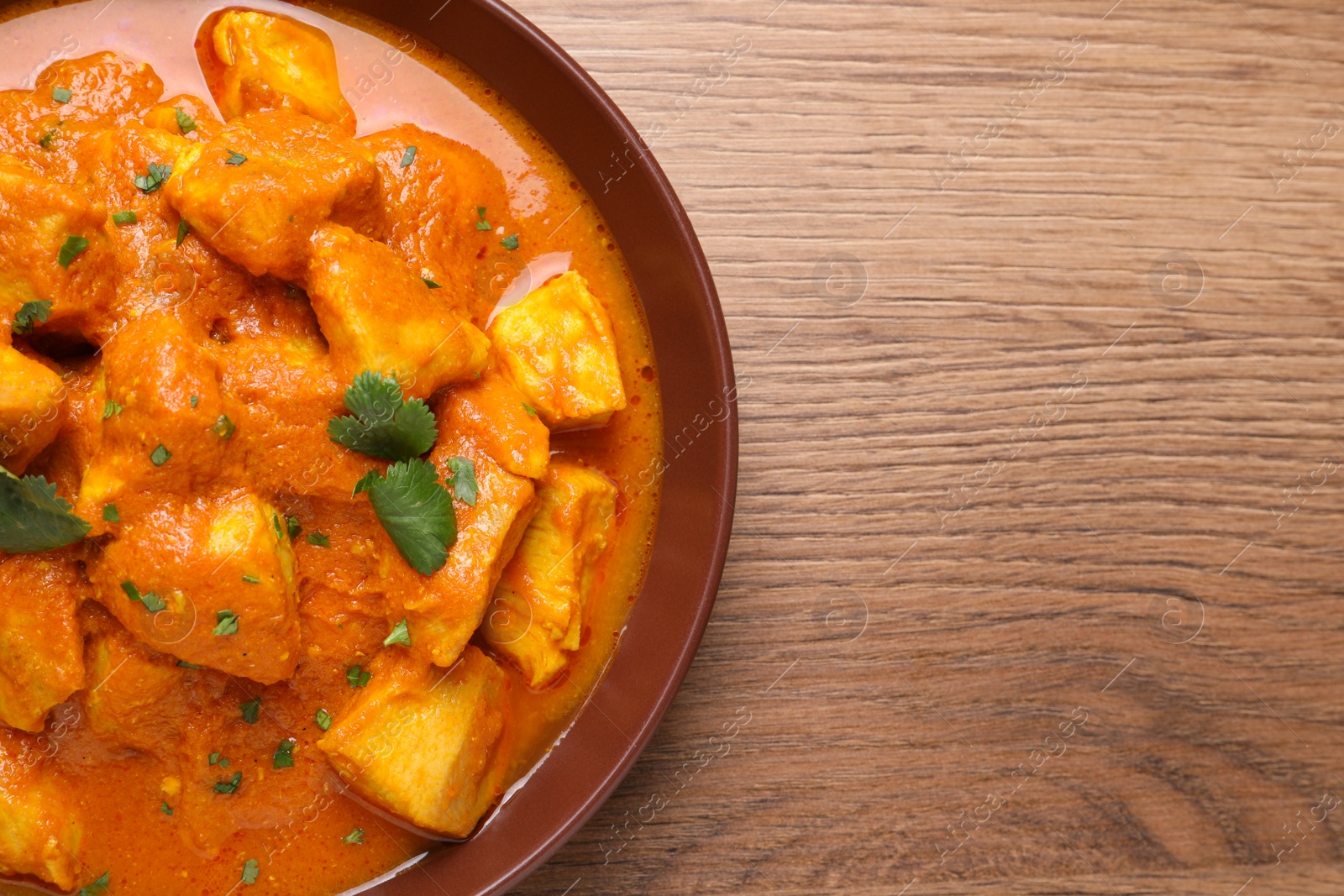 Photo of Bowl of delicious chicken curry on wooden table, top view. Space for text