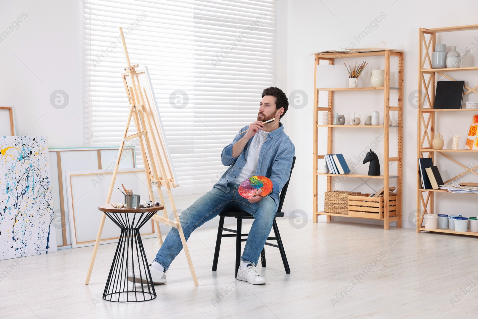 Photo of Man painting in studio. Using easel to hold canvas