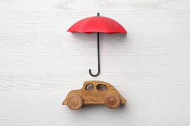 Photo of Small umbrella and toy car on white wooden background, flat lay