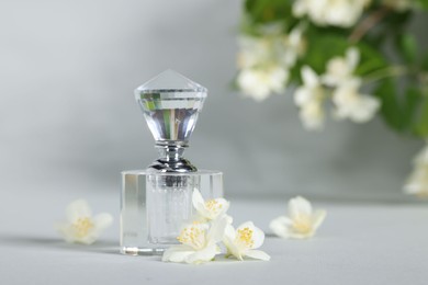 Photo of Aromatic perfume in bottle and beautiful jasmine flowers on grey background, closeup. Space for text