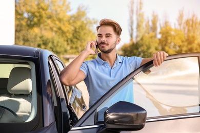 Photo of Young man talking on phone near modern car, outdoors