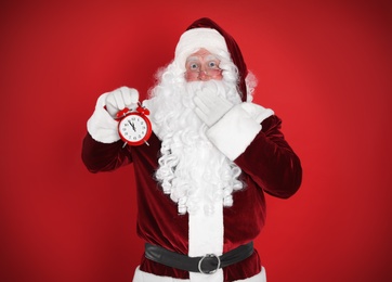 Photo of Santa Claus holding alarm clock on red background. Christmas countdown
