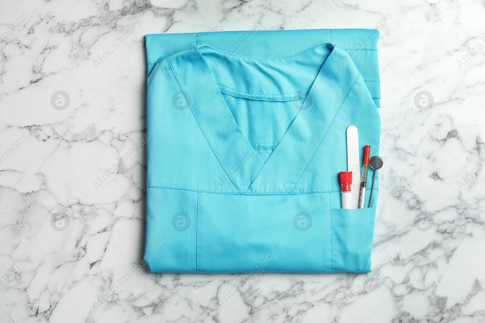 Photo of Folded uniform with medical objects in pocket on marble background, top view