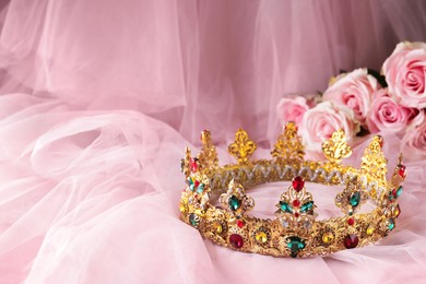 Photo of Beautiful golden crown with gems on pink cloth. Space for text
