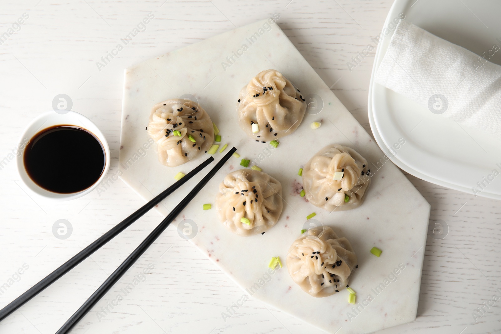 Photo of Board with tasty baozi dumplings, chopsticks and bowl of soy sauce on white wooden table, top view