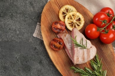 Pieces of delicious tuna steak with rosemary, tomatoes and lemon on grey table, top view. Space for text