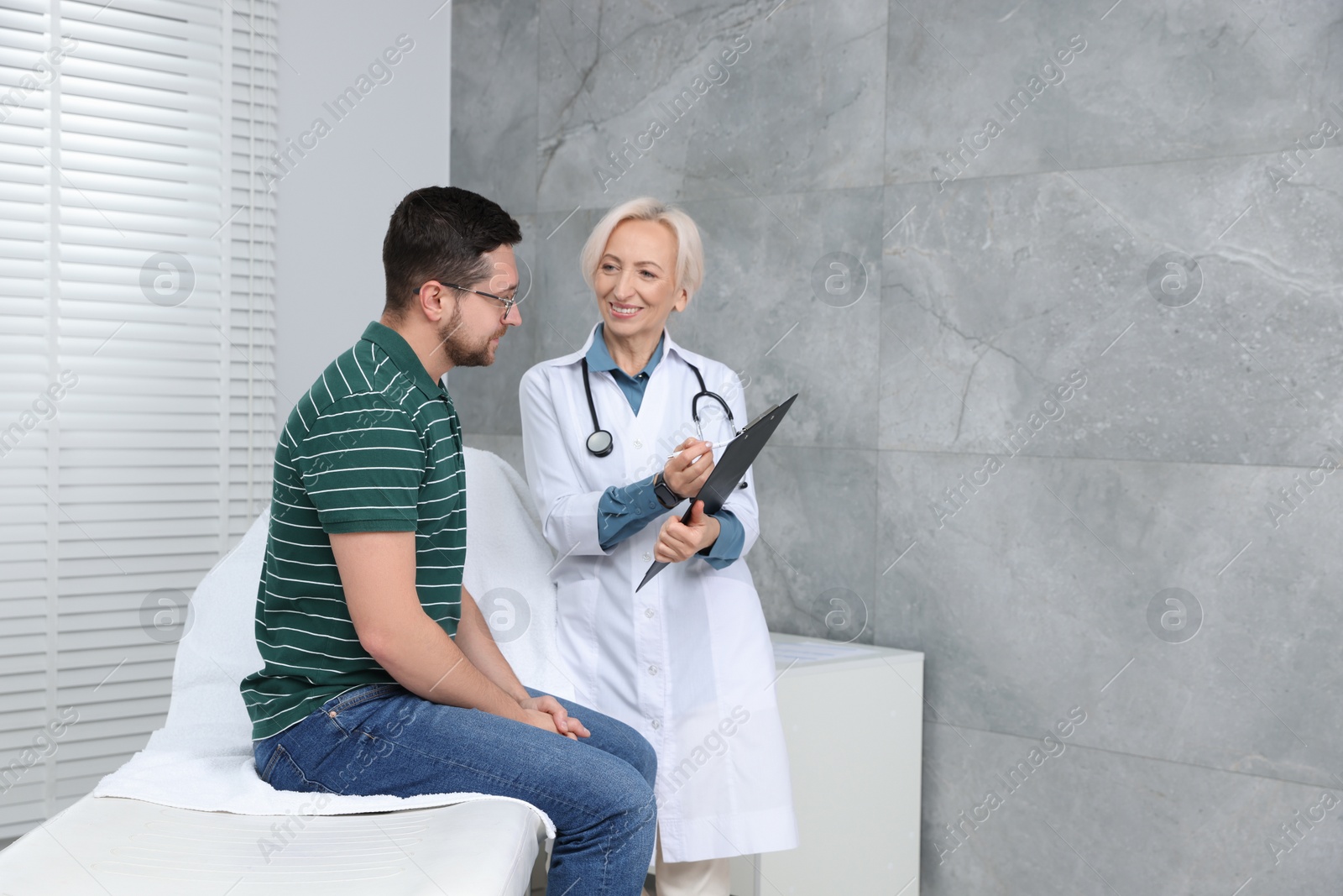 Photo of Doctor with clipboard consulting patient in clinic