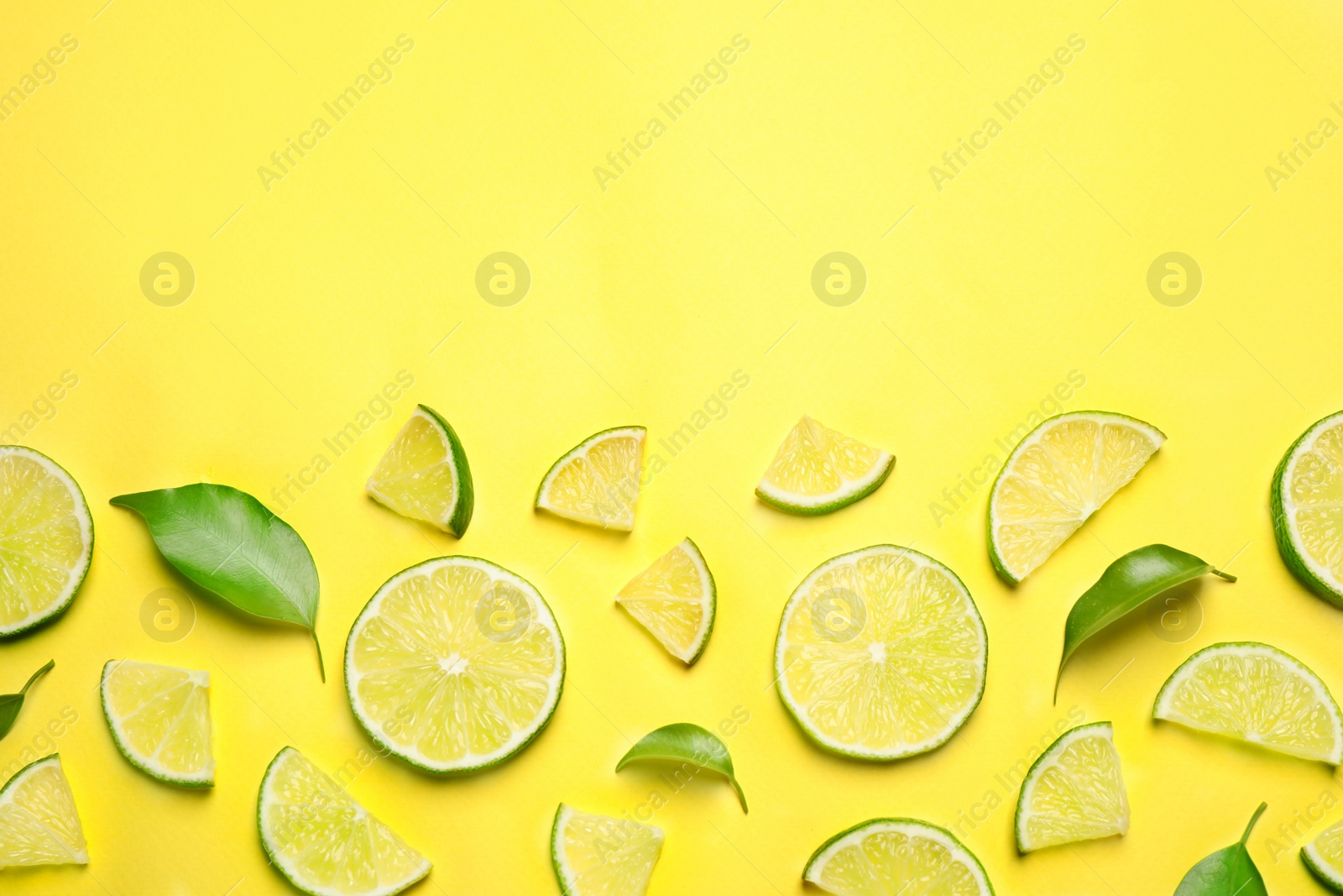 Photo of Juicy fresh lime slices and green leaves on yellow background, flat lay. Space for text