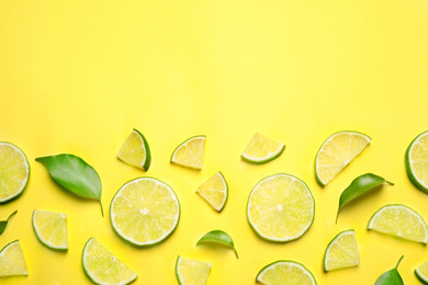 Photo of Juicy fresh lime slices and green leaves on yellow background, flat lay. Space for text