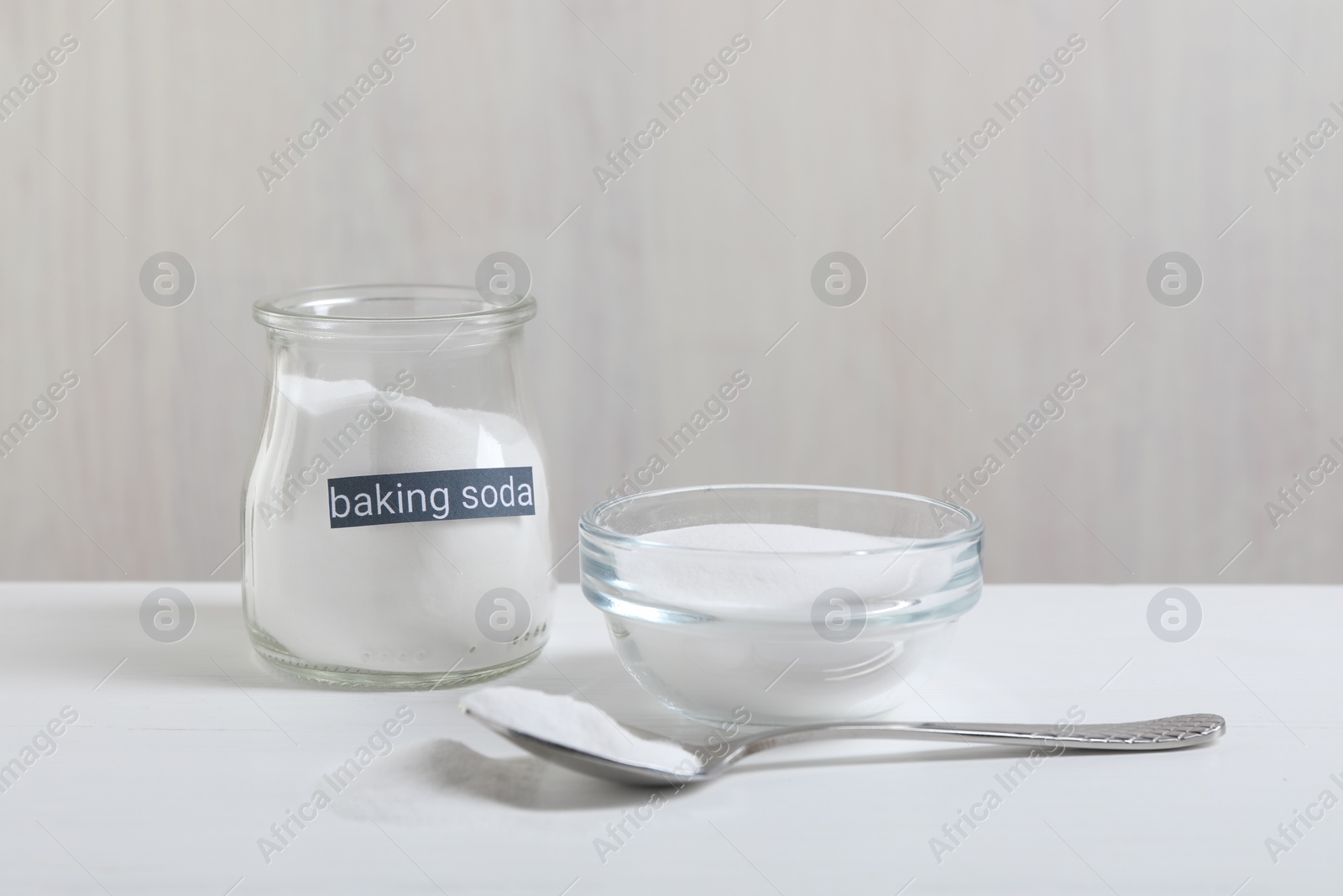 Photo of Baking soda in bowl, glass jar and spoon on white wooden table