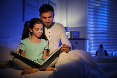 Father with little daughter reading fairy tale in dark bedroom