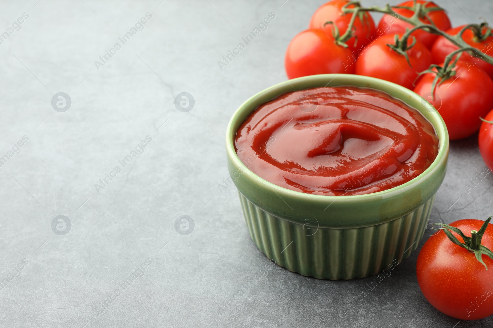 Photo of Bowl of tasty ketchup and tomatoes on light grey table, closeup. Space for text