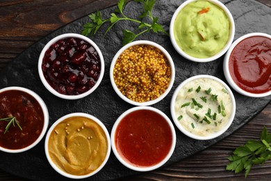 Different tasty sauces in bowls and parsley on wooden table, top view