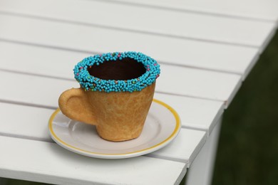 Delicious edible biscuit coffee cup decorated with sprinkles on white wooden table outdoors