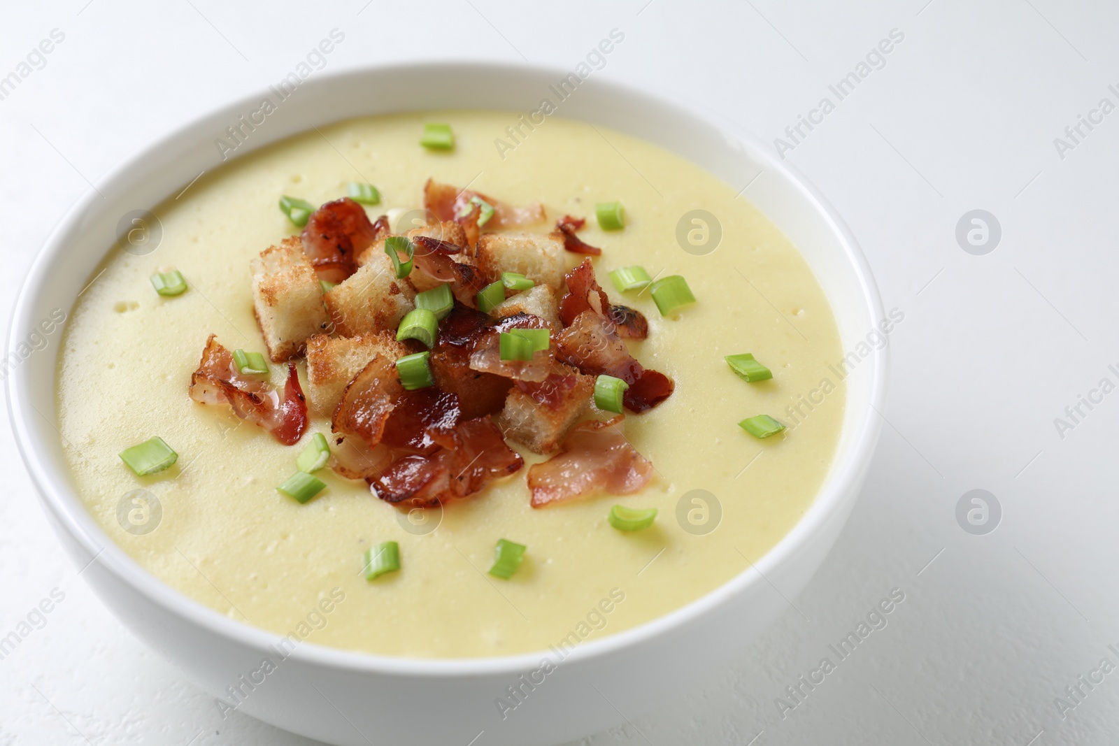 Photo of Tasty potato soup with bacon, green onion and croutons in bowl on white table, closeup