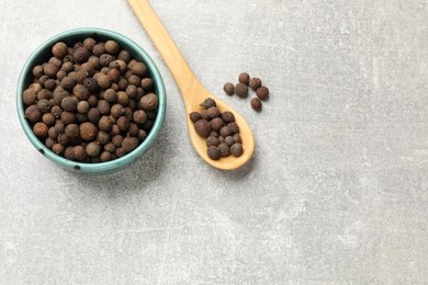Photo of Aromatic allspice pepper grains in bowl and spoon on grey table, top view. Space for text