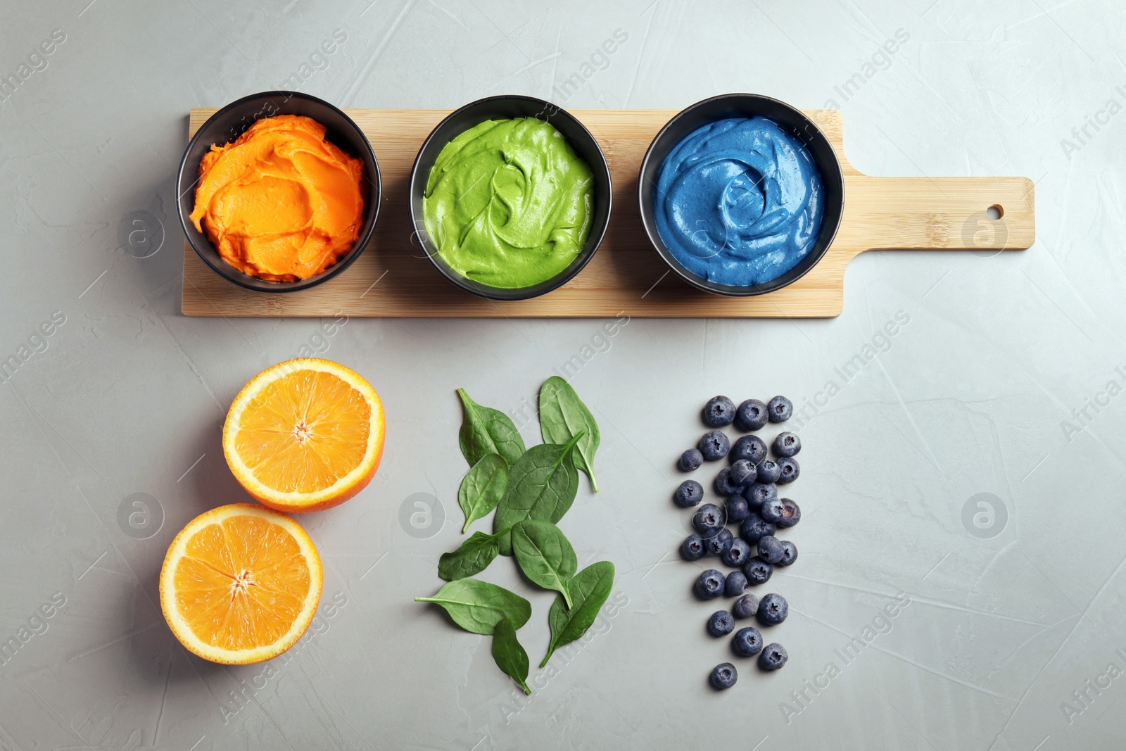 Photo of Cream painted with natural food colorings, orange, spinach and blueberries on light table, flat lay