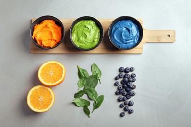 Photo of Cream painted with natural food colorings, orange, spinach and blueberries on light table, flat lay