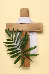 Wooden cross, white cloth and palm leaf on beige background, top view. Easter attributes