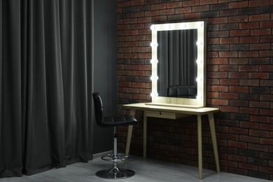 Photo of Mirror with light bulbs, table, chair and curtain in makeup room