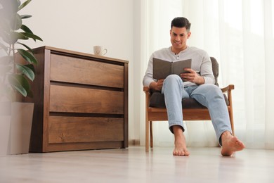 Photo of Man with book sitting in armchair at home. Floor heating system