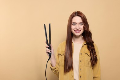 Photo of Beautiful woman with hair iron on beige background, space for text