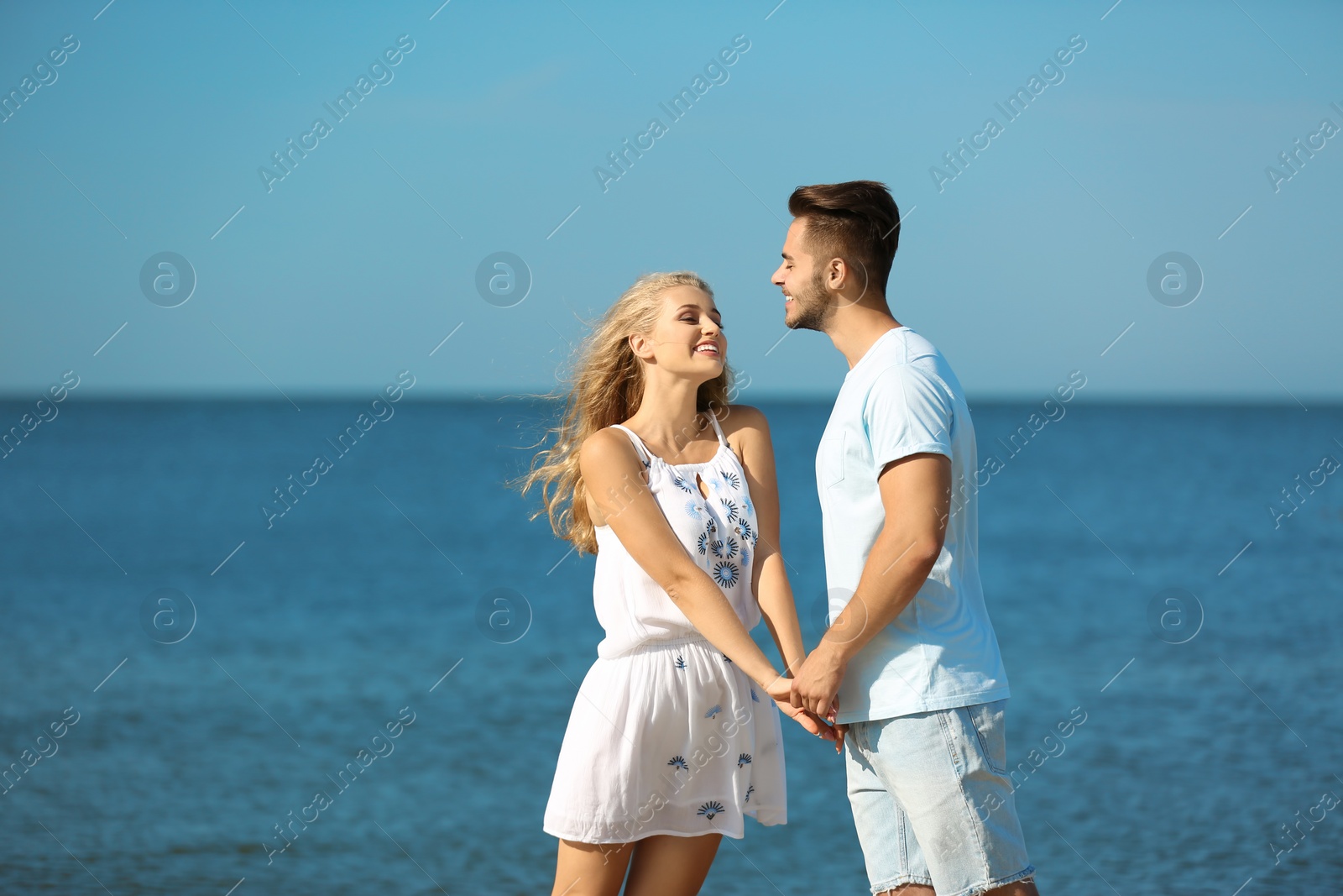 Photo of Happy young couple holding hands at beach on sunny day