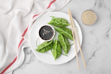 Photo of Delicious green dumplings (gyozas) and soy sauce served on white marble table, flat lay