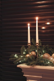 Burning candles and Christmas decor on white mantelpiece indoors
