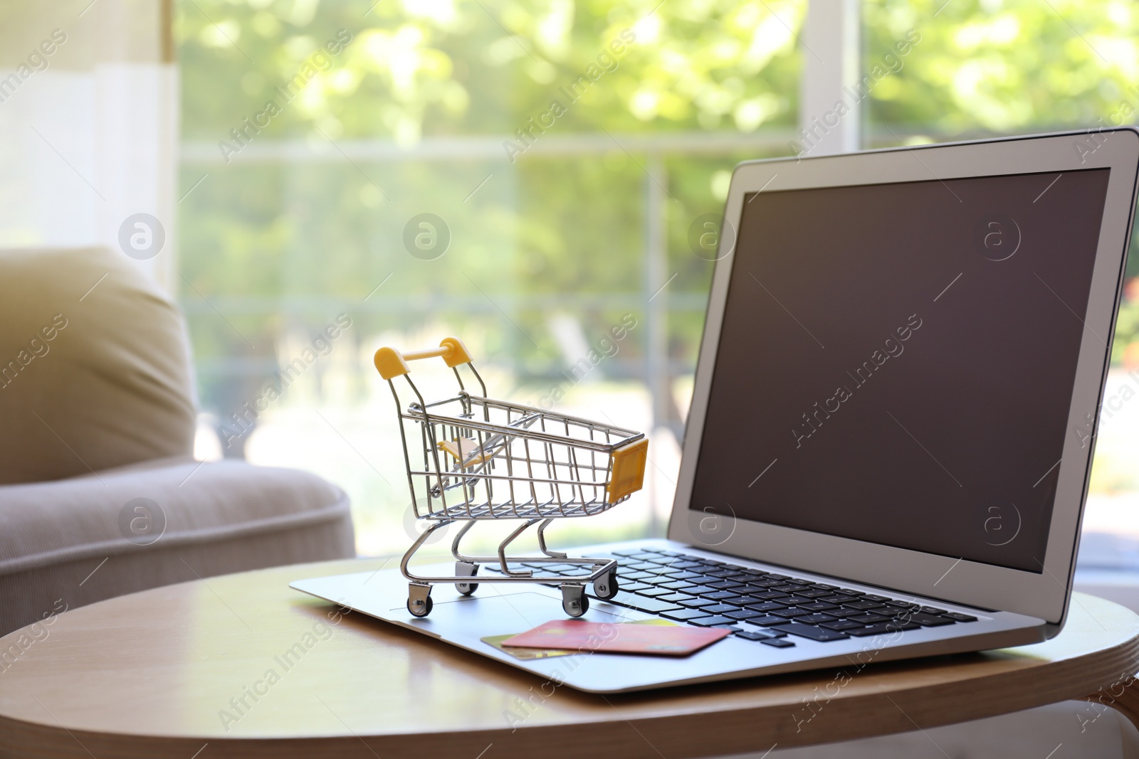 Photo of Internet shopping. Laptop, small cart and credit cards on table indoors